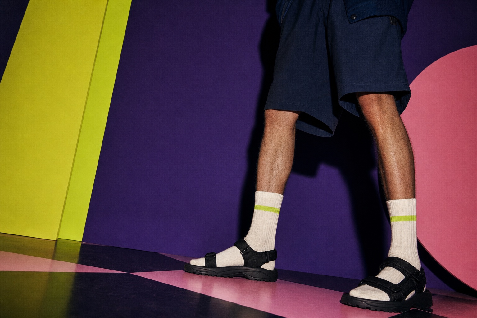 Model wearing cream crew socks with black strappy sport sandals in a purple fashion studio
