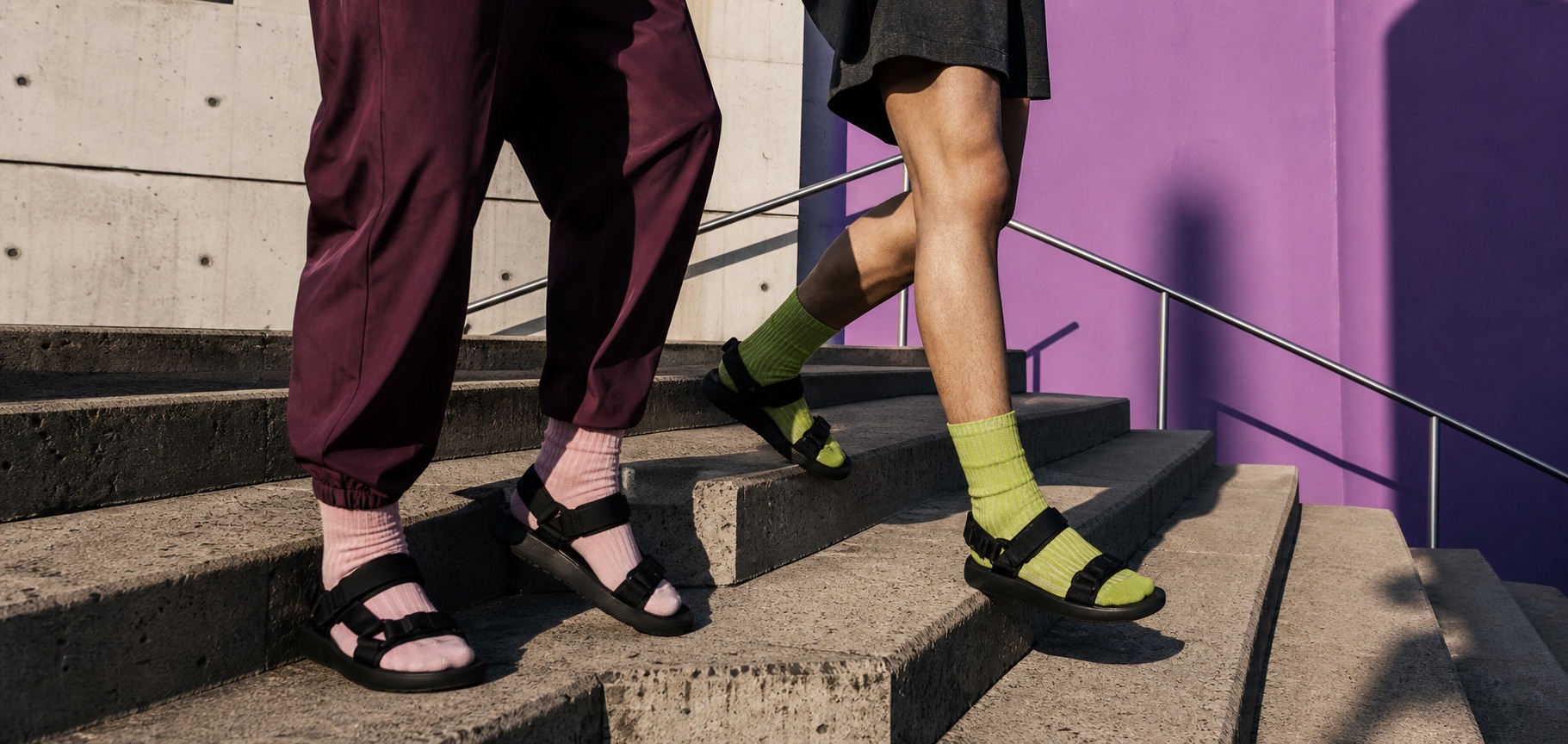 Two people wearing colorful socks with black sport sandals on downtown concrete steps